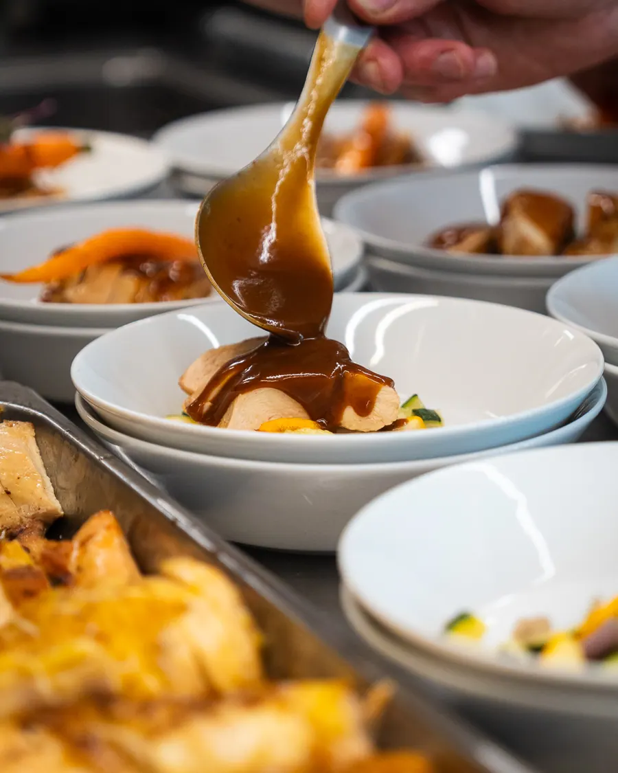 Chef schept jus over gevogelte in een diep bord
