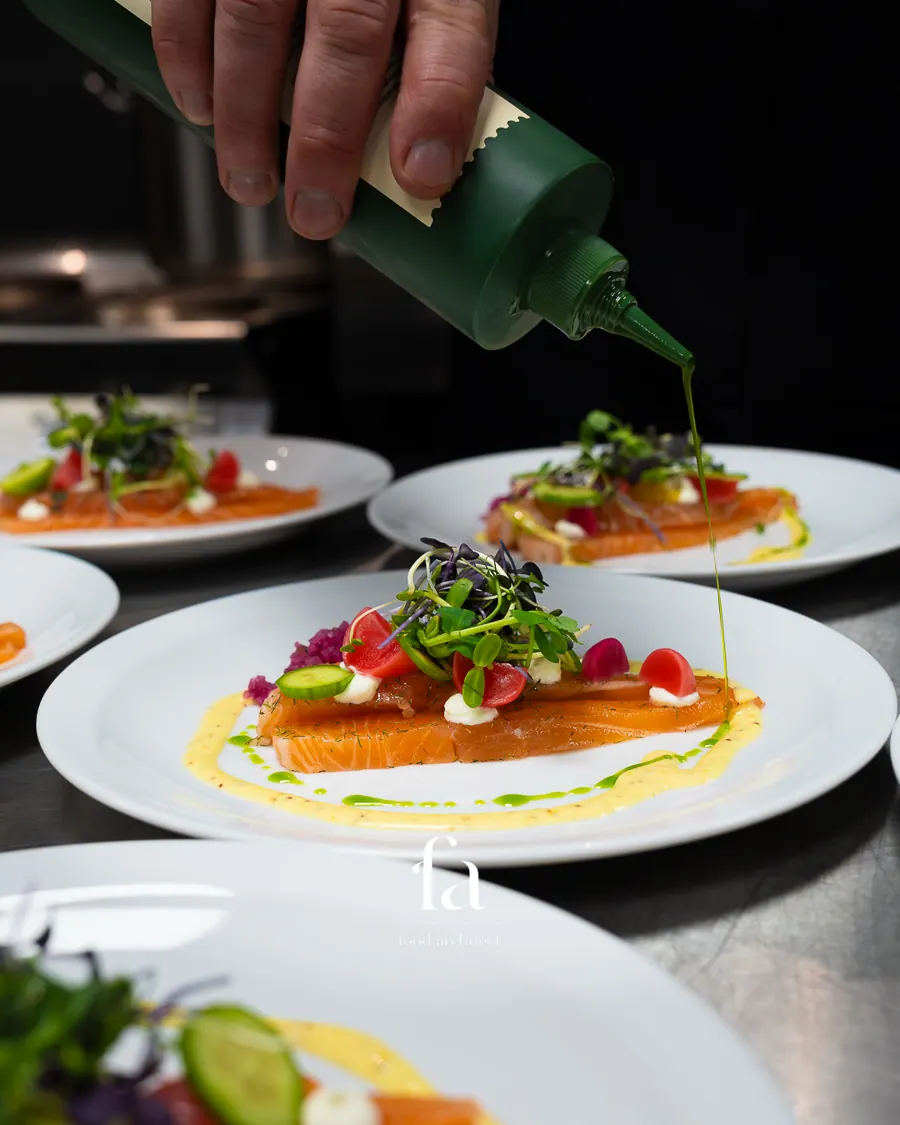 Chef giet kruidenolie over gemarineerde zalm met microgroenten